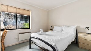 Un dormitorio con cama, mesitas de noche, un escritorio y una ventana con persianas.