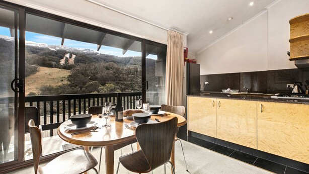 Un comedor con una mesa preparada para dos, una cocina con electrodomésticos modernos y vistas panorámicas de un paisaje montañoso a través de amplios ventanales.