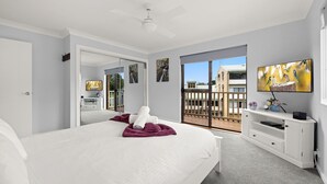 A bedroom with a large bed, a TV, and a balcony with a view of buildings.