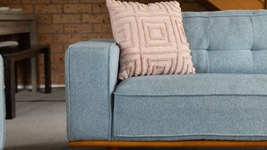 A blue sofa with a wooden base and a textured pink pillow.