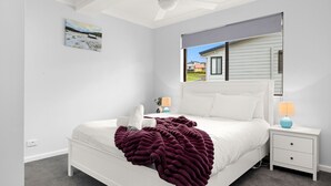 A bedroom with a bed, a nightstand, a lamp, and a window with a view of a house.
