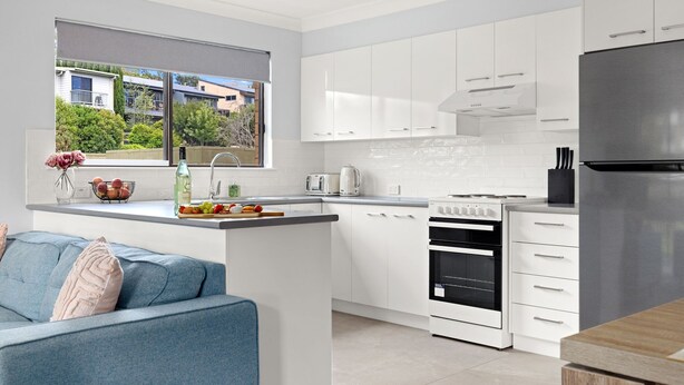 A modern kitchen with white cabinetry, a built-in oven, and a stainless steel refrigerator.