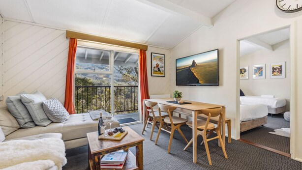 Een gezellige kamer met een bank, een eettafel met stoelen, een bed en een groot raam met uitzicht.