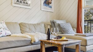 Een gezellige woonkamer met een bank, een houten salontafel met een fles wijn en glazen, en decoratieve kussens.