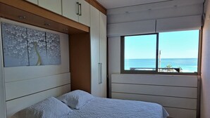 Um quarto com uma cama, uma janela com vista para o mar e uma parede com um desenho floral.