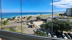 Vista de um estacionamento com vários carros, uma praia e um edifício ao fundo.