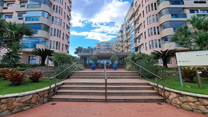Um edifício de apartamentos moderno com fachada curva, parede de pedra e uma placa indicando 'Ocean Drive' e 'Bloco 1'.