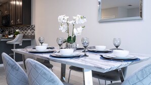 A dining area with a marble table, white chairs, and a vase of white flowers.
