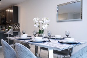 Uma área de refeições com uma mesa de mármore, cadeiras brancas e um vaso de flores brancas.