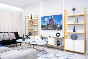 Enjoy a stylish living room featuring plush gray sofas and a chic coffee table, perfect for relaxation. Unique shelving showcases modern decor, while bright walls and natural light create an uplifting atmosphere for your stay.
