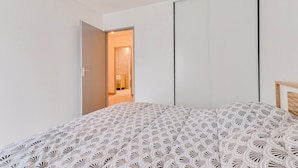 Ein Schlafzimmer mit Bett, Kleiderschrank und offener Tür zu einem anderen Raum.