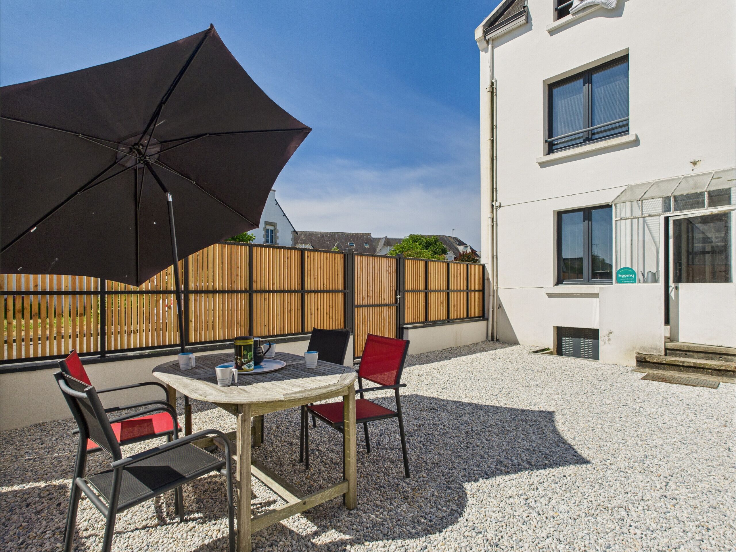 An outdoor patio with a table and chairs, a black umbrella, and a wooden fence.