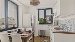 A compact kitchen with a dining area, a refrigerator, a sink, and a window with blinds.