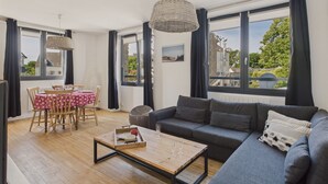 A modern living room with a grey sofa, wooden coffee table, and a dining area with a red star-patterned tablecloth.