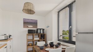 A compact kitchen with a wooden table, white chairs, a built-in microwave shelf, and a window with blinds.
