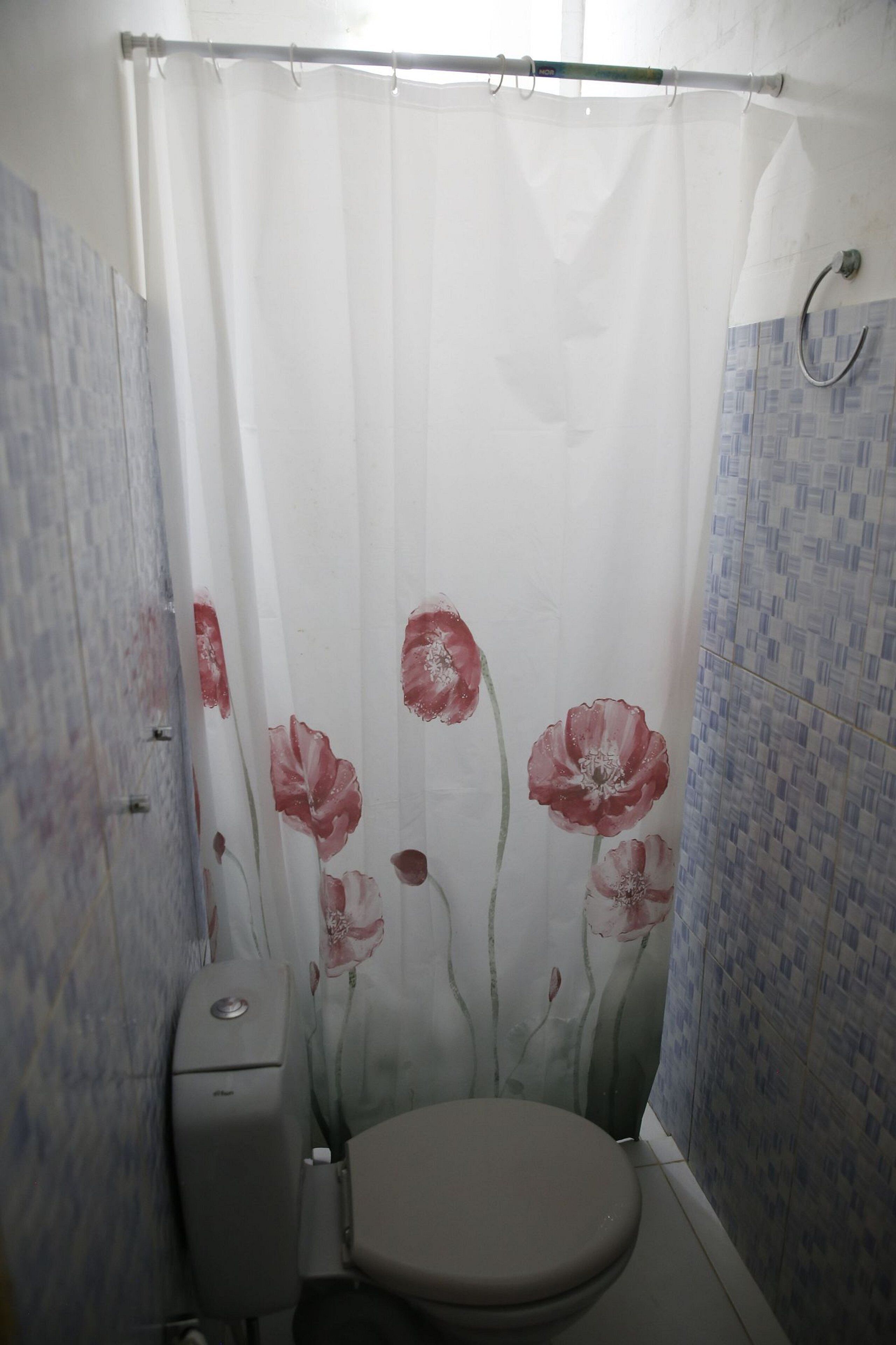 Un bany amb vàter, cortina de dutxa amb disseny floral i parets revestides de rajola.