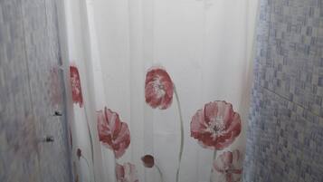Un bany amb vàter, cortina de dutxa amb disseny floral i parets revestides de rajola.