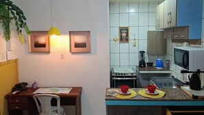 A compact kitchen with a dining area, featuring a stove, microwave, and a small island with red cups. - paratemporada (Belém)