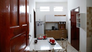 A compact kitchen with white cabinets, a refrigerator, and a dining table set with red cups and plates. - paratemporada (Belém)