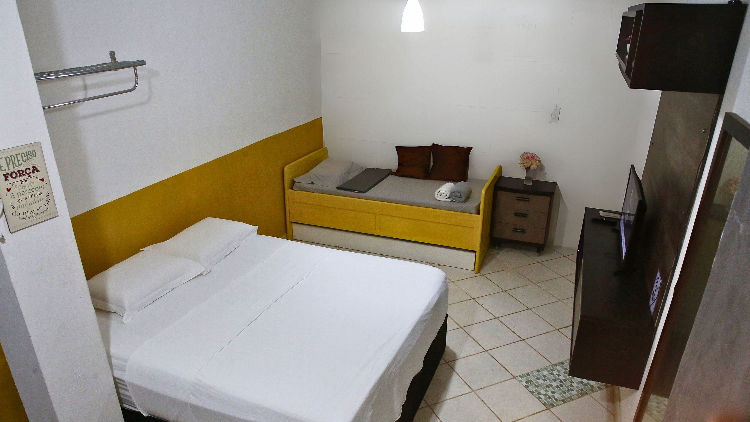 Una habitación con una cama, una mesita de noche, una pequeña mesa con una lámpara y un televisor.