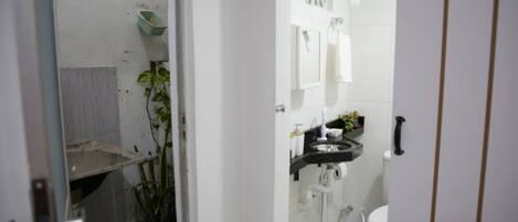 A bathroom with a toilet, sink, and towel rack. There is a plant in a corner and a shelf with toiletries.