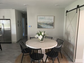 A modern kitchen with white cabinets, a stainless steel refrigerator, and a dining area with a round table and black chairs. - Vanderbilt Beach North Naples, FL - 4 Bedroom, 3 Bath Home Steps From The Beach (Naples)