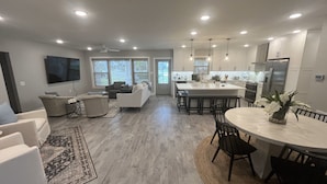Un salon moderne avec un canapé, des fauteuils et une table basse. On y trouve également un coin cuisine avec une table à manger et des chaises, ainsi qu’un grand îlot central.