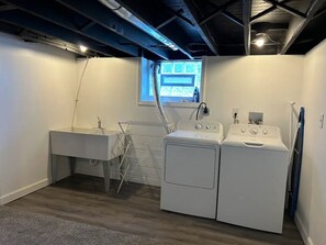 Laundry room with a sink, drying rack, and two washing machines, offering a view of the surrounding building.