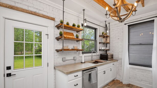 Une cuisine moderne avec des murs en briques blanches, des poutres en bois et un lave-vaisselle encastré.