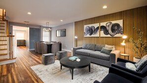 A modern living room with a grey sofa, black coffee table, and a wooden accent wall. - The Lambertville Haven (Lambertville)