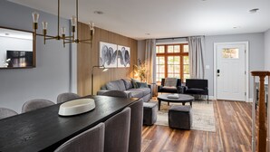 A modern living room with a dining area, featuring a wooden floor, grey sofas, and a large painting on the wall. - The Lambertville Haven (Lambertville)