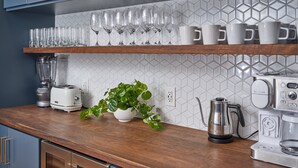A modern kitchen with grey cabinets, a wooden countertop, a coffee machine, a kettle, and a plant. - The Lambertville Haven (Lambertville)
