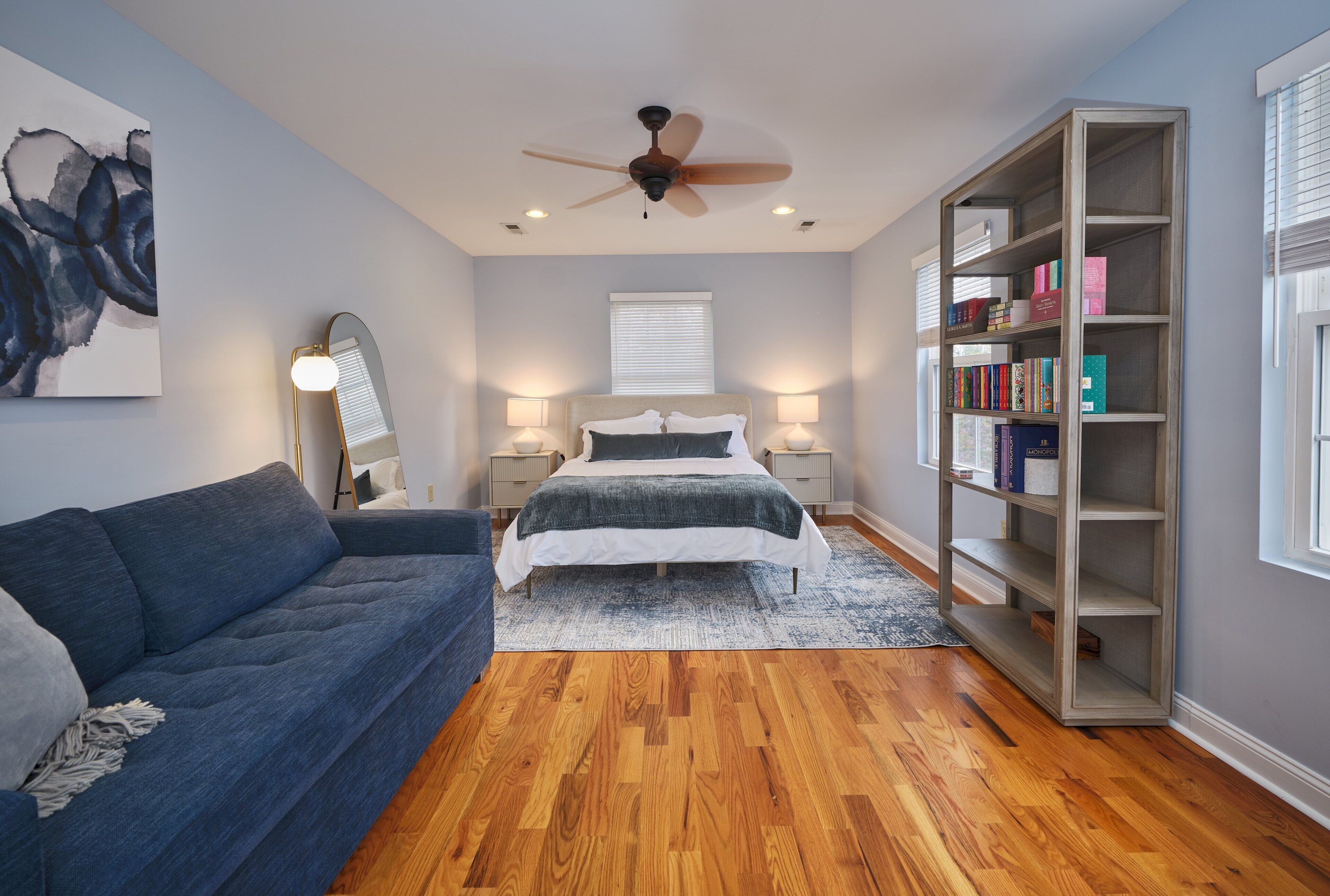 A bedroom with a bed, a blue sofa, a bookshelf, and a ceiling fan.