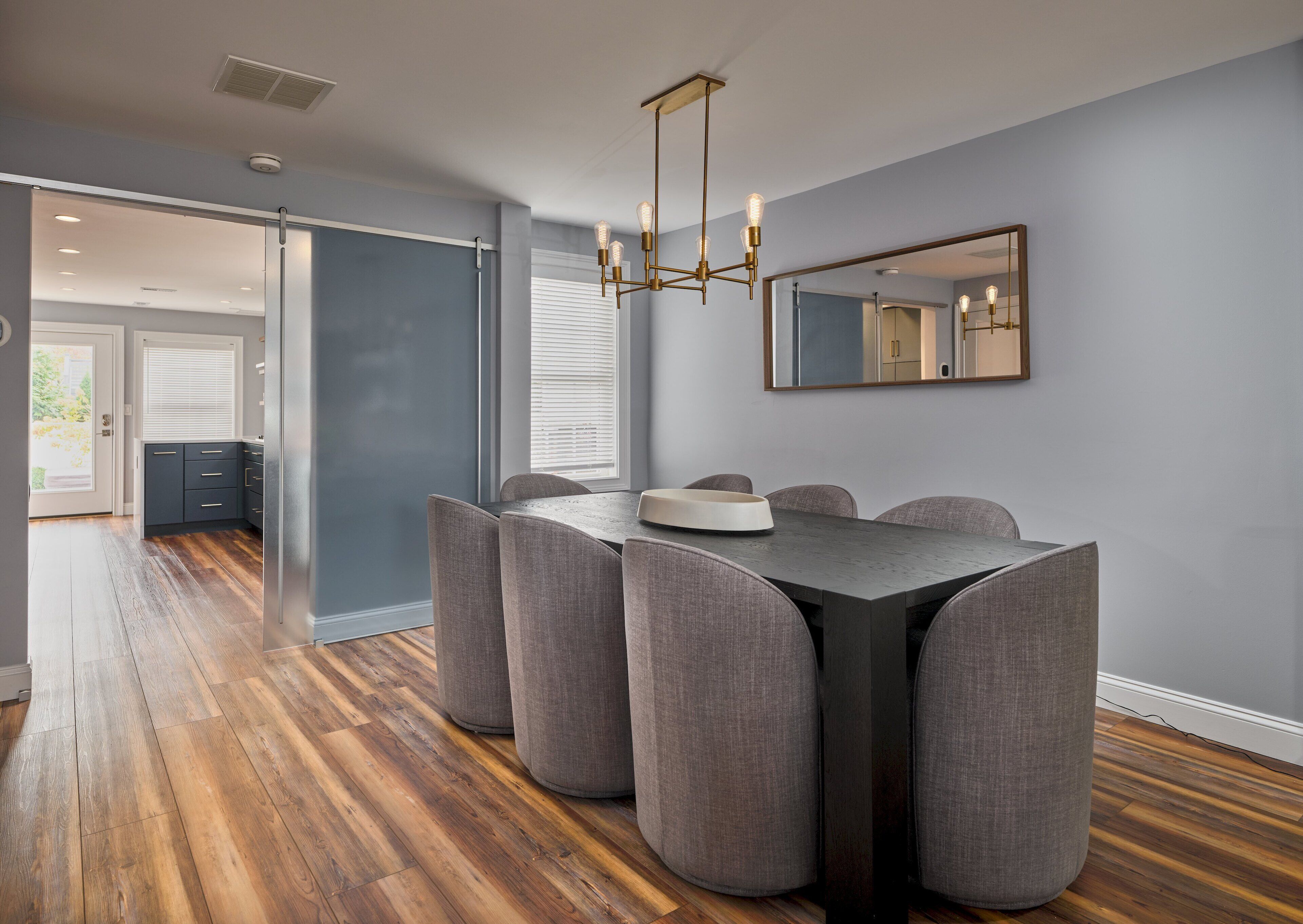 A dining area with a dark table, grey upholstered chairs, and a modern chandelier.