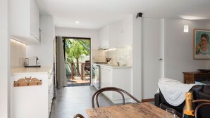 Eine moderne Küche mit weißen Schränken, ein Essbereich mit einem Holztisch und Blick auf eine tropische Außenanlage.