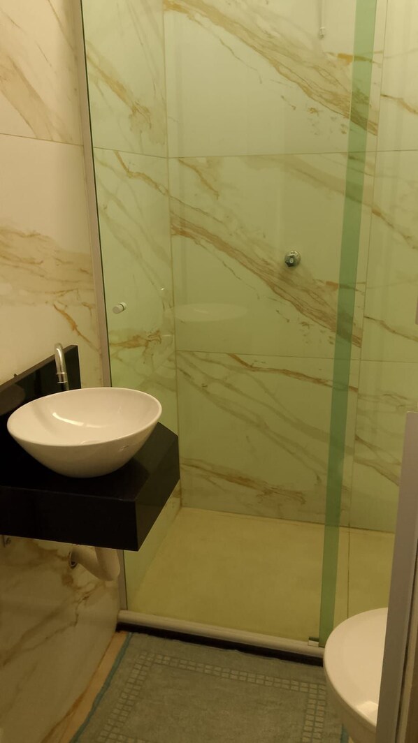 Een badkamer met een marmeren wand, een witte wastafel en een glazen douchecabine.