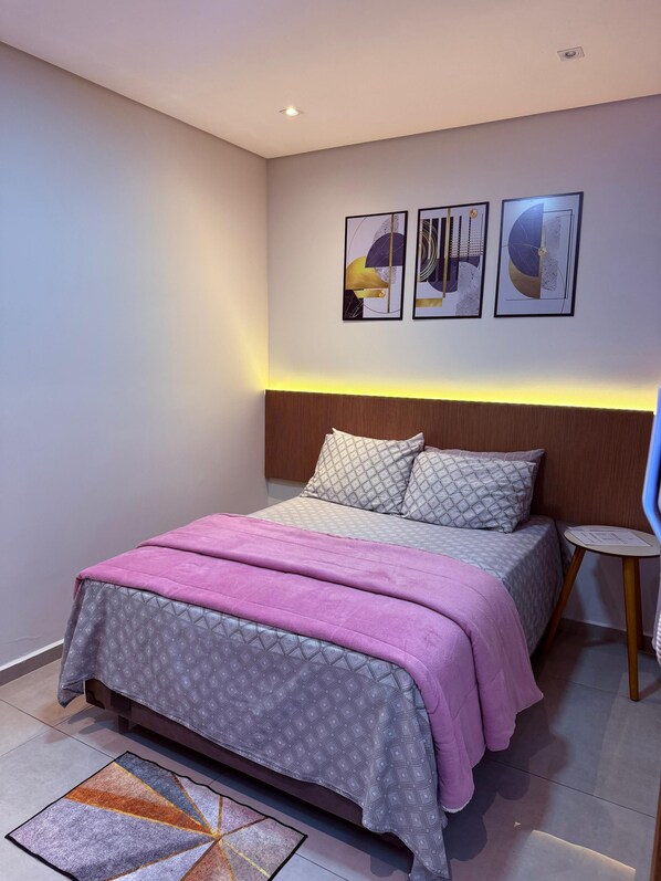 Un dormitorio moderno con cama, cabecero, mesita de noche y arte abstracto en la pared.