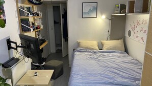 A compact bedroom with a bed, bedside table, and a desk with a computer. - Studio Confortable Paris 13 (Paris)