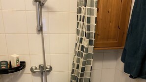 A small bathroom with a shower, toilet, and a shelf with toiletries. - Studio Confortable Paris 13 (Paris)
