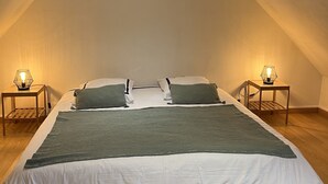 Un dormitorio abrigado y bien iluminado en el ático, con techo inclinado, una cama grande con ropa de cama verde, dos lámparas de noche y suelo de madera.