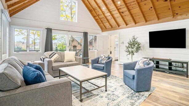 A spacious living room with a high ceiling, large windows, and a flat-screen TV. - Park Place: Luxury Riverfront Home, Walk to Lake Michigan & Chain Ferry, Deck (Saugatuck)