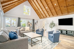 A spacious living room with a high ceiling, large windows, and a flat-screen TV.