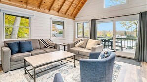 A spacious living area with a high wooden ceiling, large windows, and a view of a lake. - Park Place: Luxury Riverfront Home, Walk to Lake Michigan & Chain Ferry, Deck (Saugatuck)