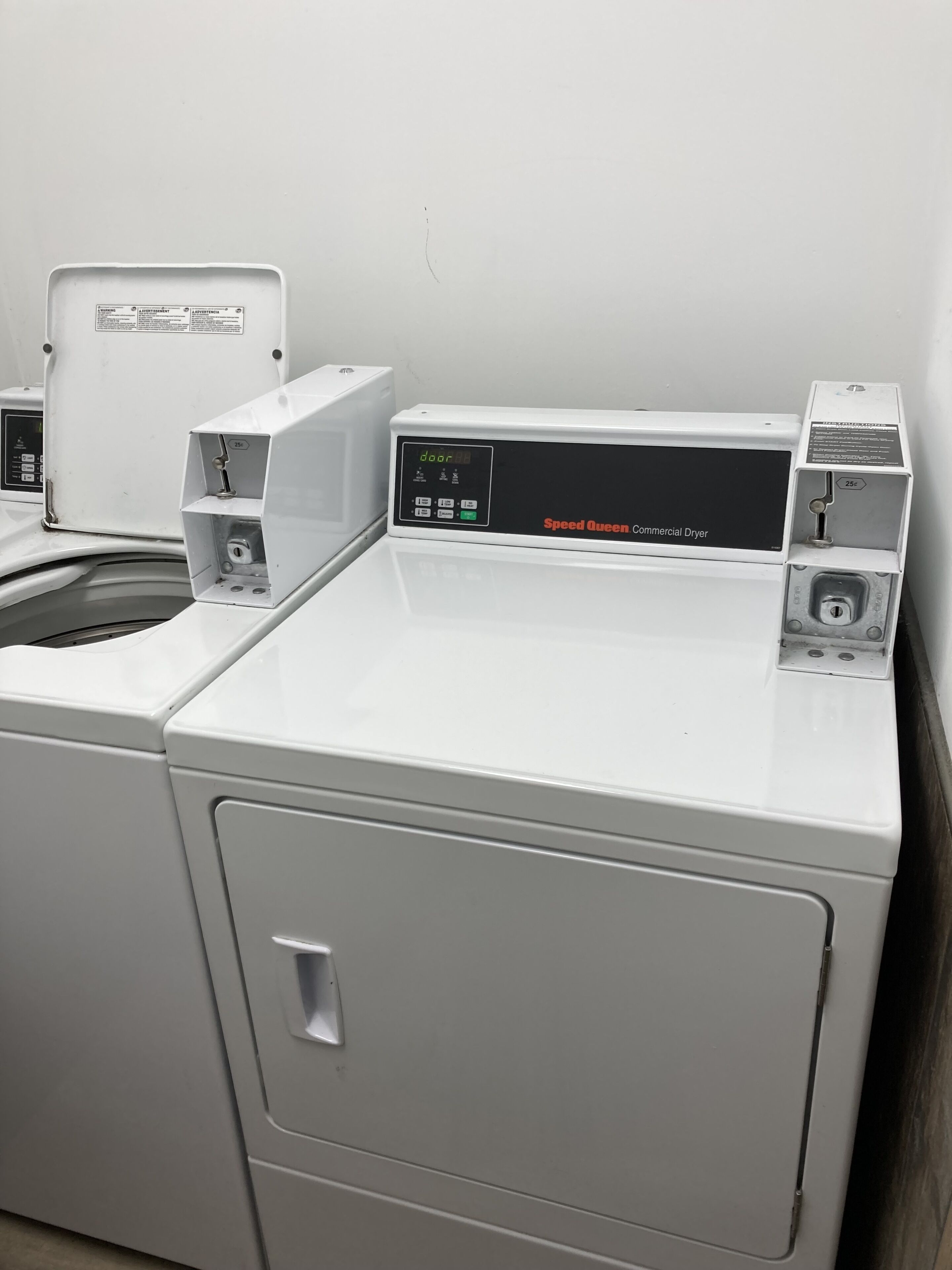 Uma secadora Speed Queen comercial com painel de controle, porta e compartimento para moeda de 25 centavos.
