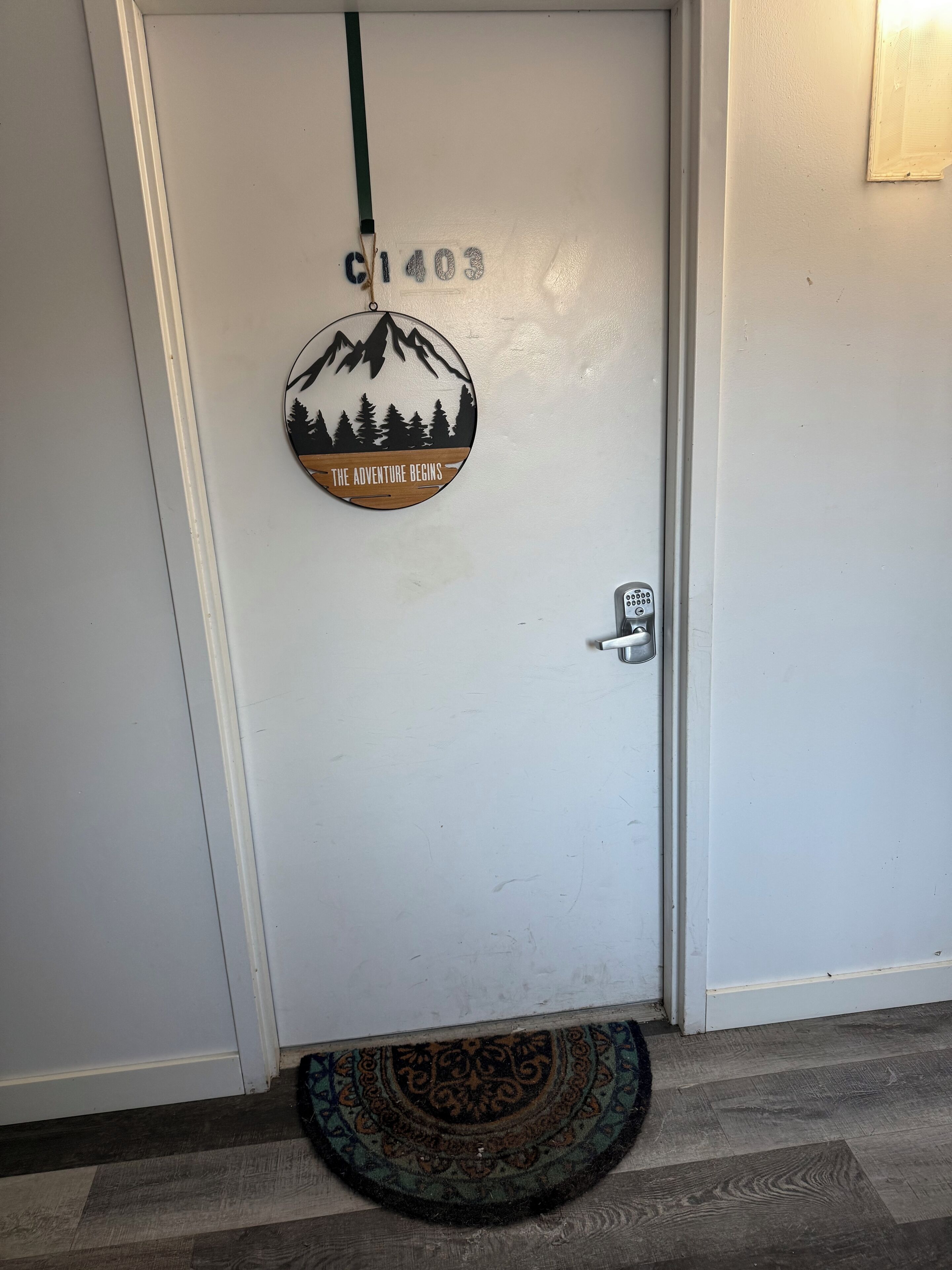 Une porte blanche sur laquelle est apposé un panneau circulaire portant l’inscription « L’AVENTURE COMMENCE » et, au-dessus, le numéro « C1403 ».