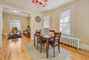 A dining area with a wooden table and chairs, a clock on the wall, and a radiator.