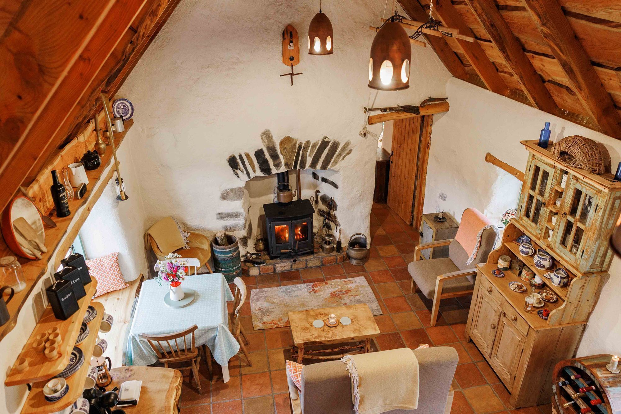 A cozy, rustic interior with a stone fireplace, wooden furniture, and a high ceiling with exposed beams.