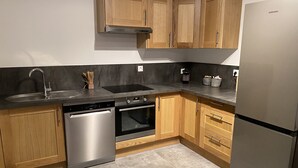 Une cuisine moderne avec des meubles en bois, des appareils électroménagers en acier inoxydable et un sol carrelé de couleur grise.