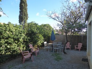Relax in a serene outdoor setting with a table and chairs surrounded by lush greenery and a shaded area.