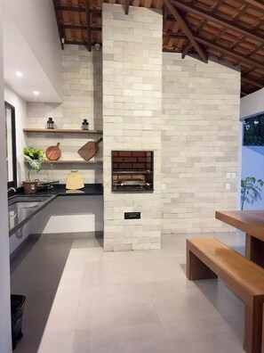 Una cocina moderna con chimenea empotrada, paredes de piedra, estantes de madera y una zona de comedor con banco.